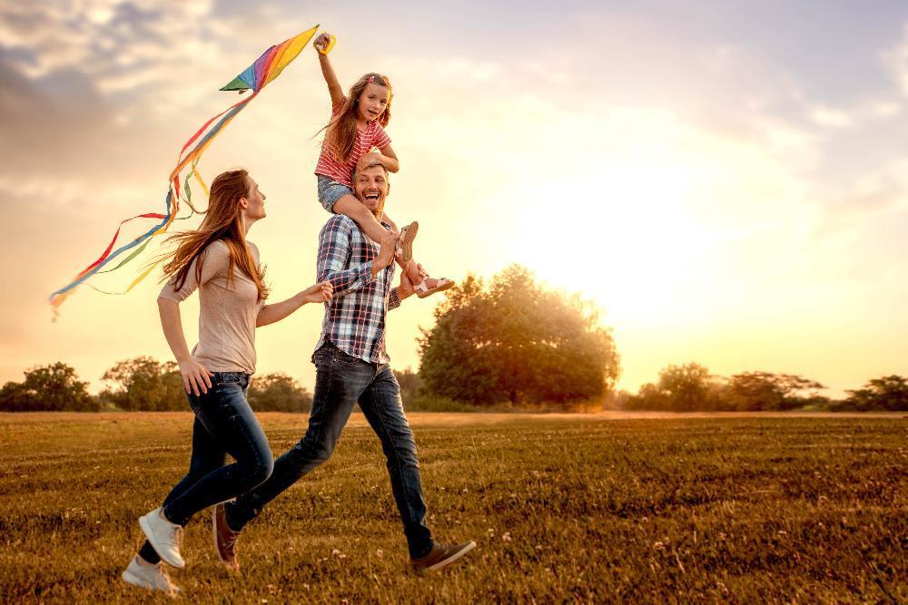 mom and dad with daughter on shoulders running through field with kite
